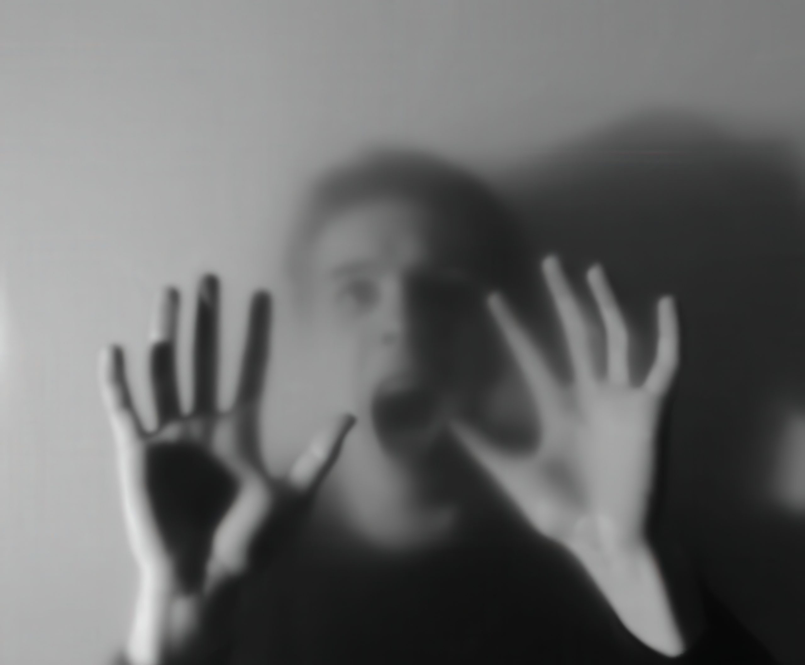 vecteezy_person-in-distress-behind-foggy-glass-expressing-fear-at-night_65867554 A blurred black-and-white image of a person behind foggy glass, pressing their hands against it and appearing to scream in distress. The visual conveys fear, anxiety, or psychological struggle, with strong emotional intensity.