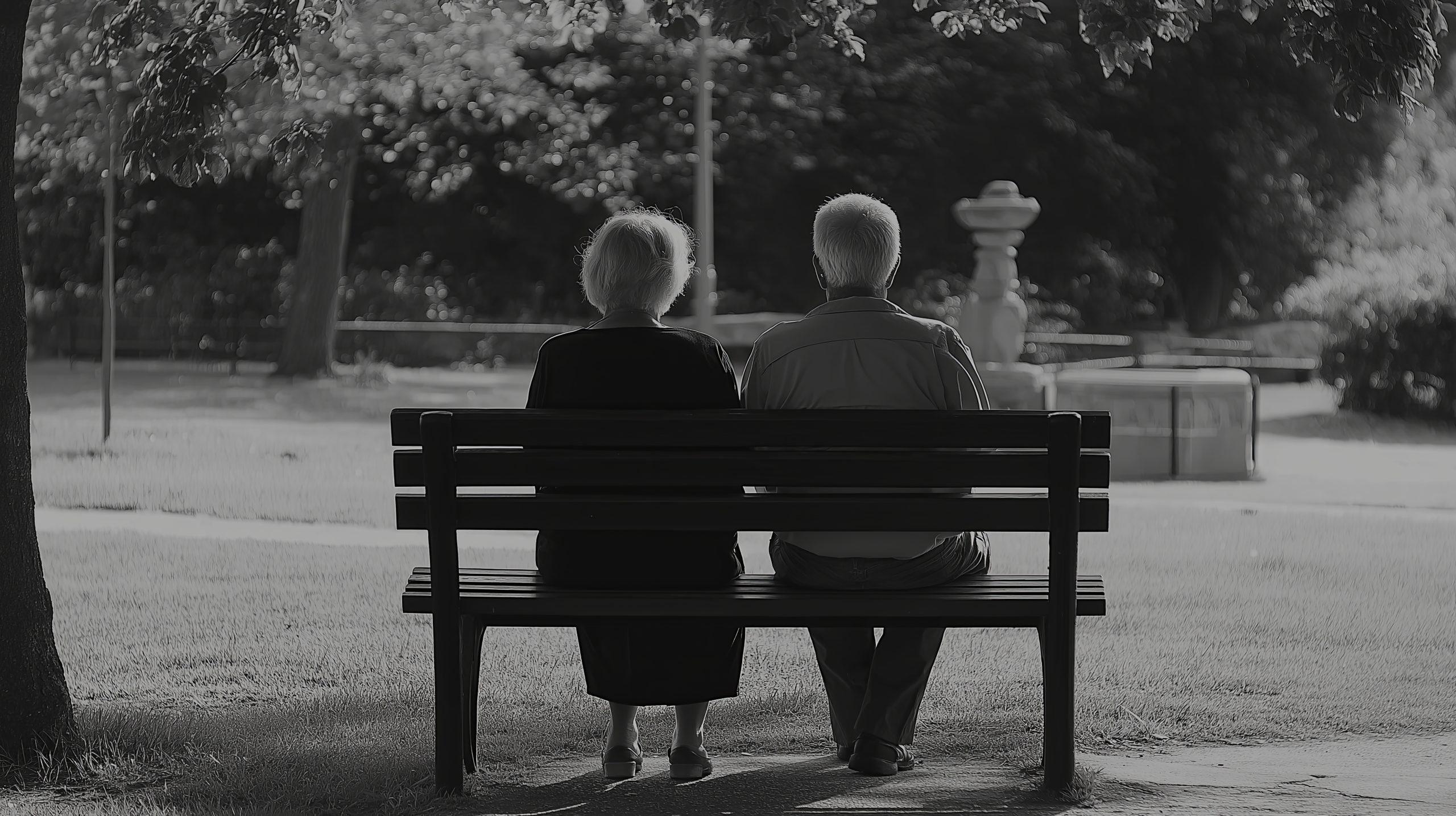A nostalgic black and white photograph of an elderly couple sitting together on a park bench, symbolizing love, companionship, and aging. Two people sitting on a bench-couples counselling Rudgwick RH 12 West Sussex