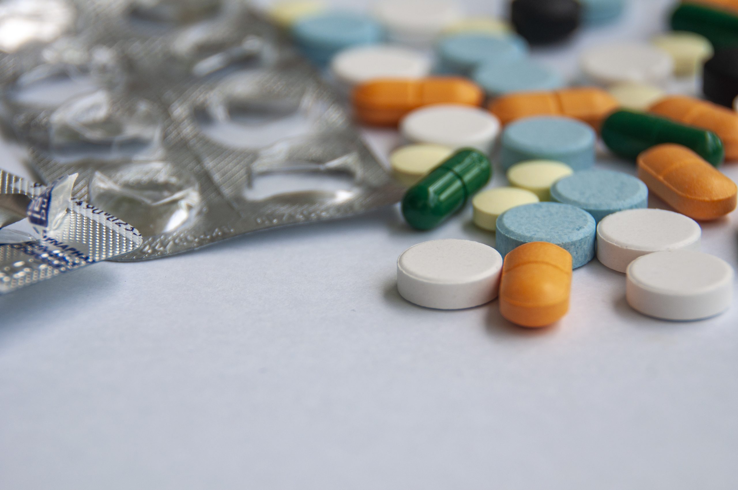 Variety of colorful pills and capsules scattered on a light colored surface with customizable space for text. Eleos Counselling; counselling for prescription drug addiction with Sussex
