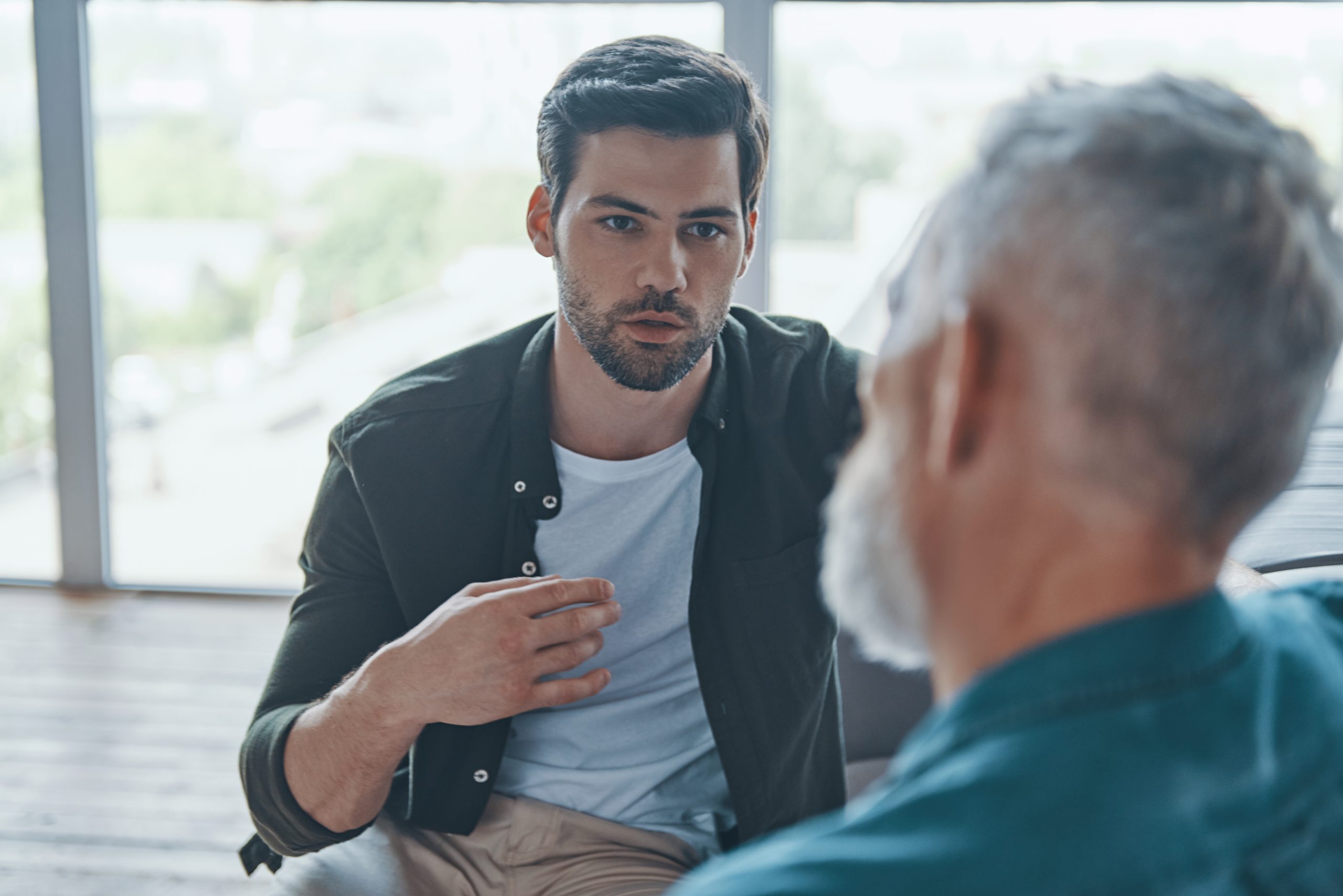 Handsome young man talking to his senior father while spending time at home together Psychotherapy counselling for men in West Sussex Eleos Counselling